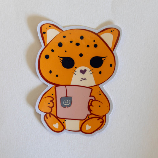 A die-cut sticker featuring a cute kawaii orange cat jaguar character with black spots, holding a pink mug, shown on a plain off-white background.
