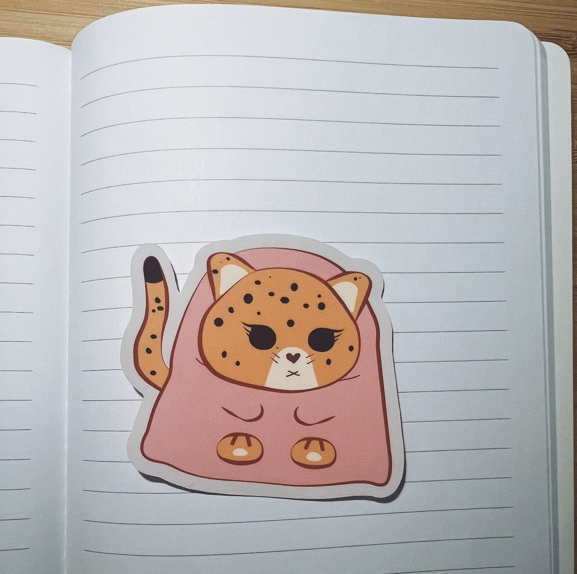 Sticker of a jaguar in a pink blanket on lined notebook paper