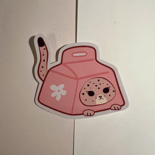 A die-cut sticker featuring a cute pink cat-shaped milk carton with a spotted leopard face and a flower detail, shown on a light beige background.