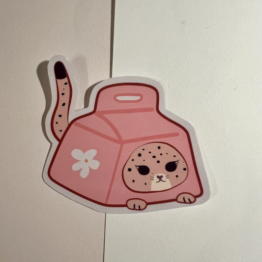 A die-cut sticker featuring a cute pink cat-shaped milk box with a spotted jaguar face, a white flower on the side, and a spotted tail, shown on a light beige background.