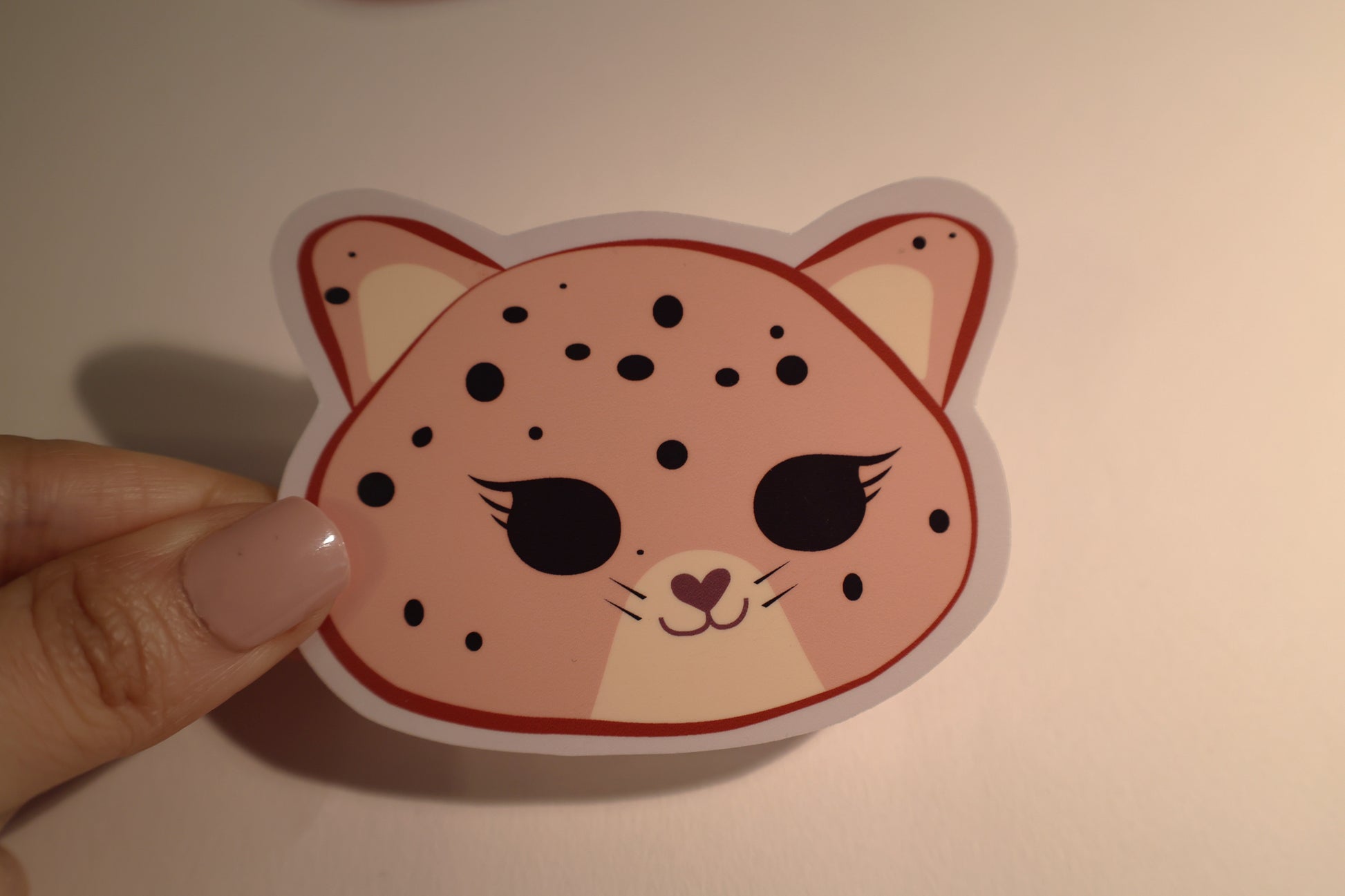 Sticker of a jaguar face held by a hand on a plain background