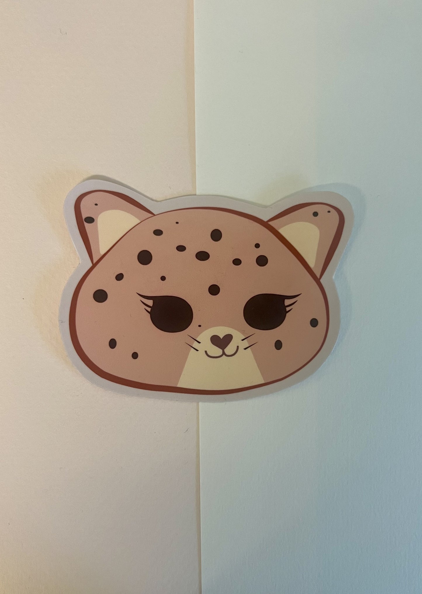 Sticker of a pink jaguar face with dot spots on a two-tone background
