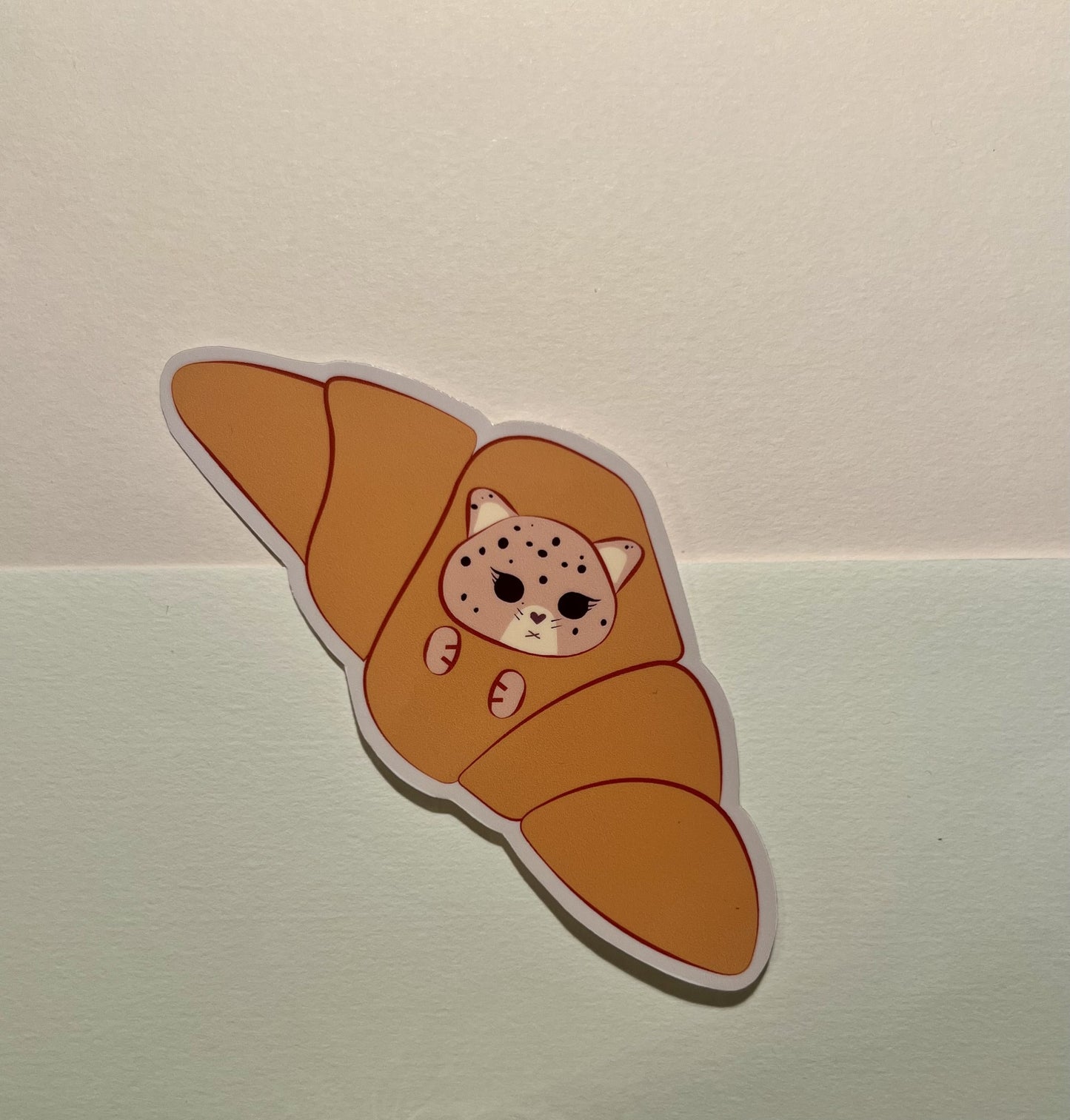 Sticker of a kawaii jaguar inside a croissant on a light background
