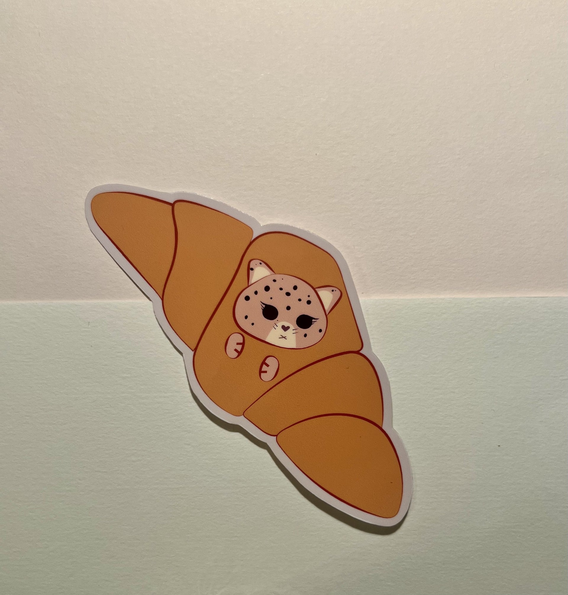Sticker of a kawaii jaguar inside a croissant on a light background
