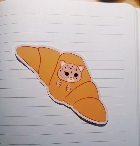 Die-cut Sticker of a cat jaguar inside a croissant on lined notebook paper