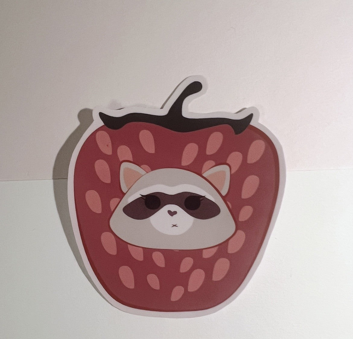 Sticker of a raccoon inside a strawberry on a white background