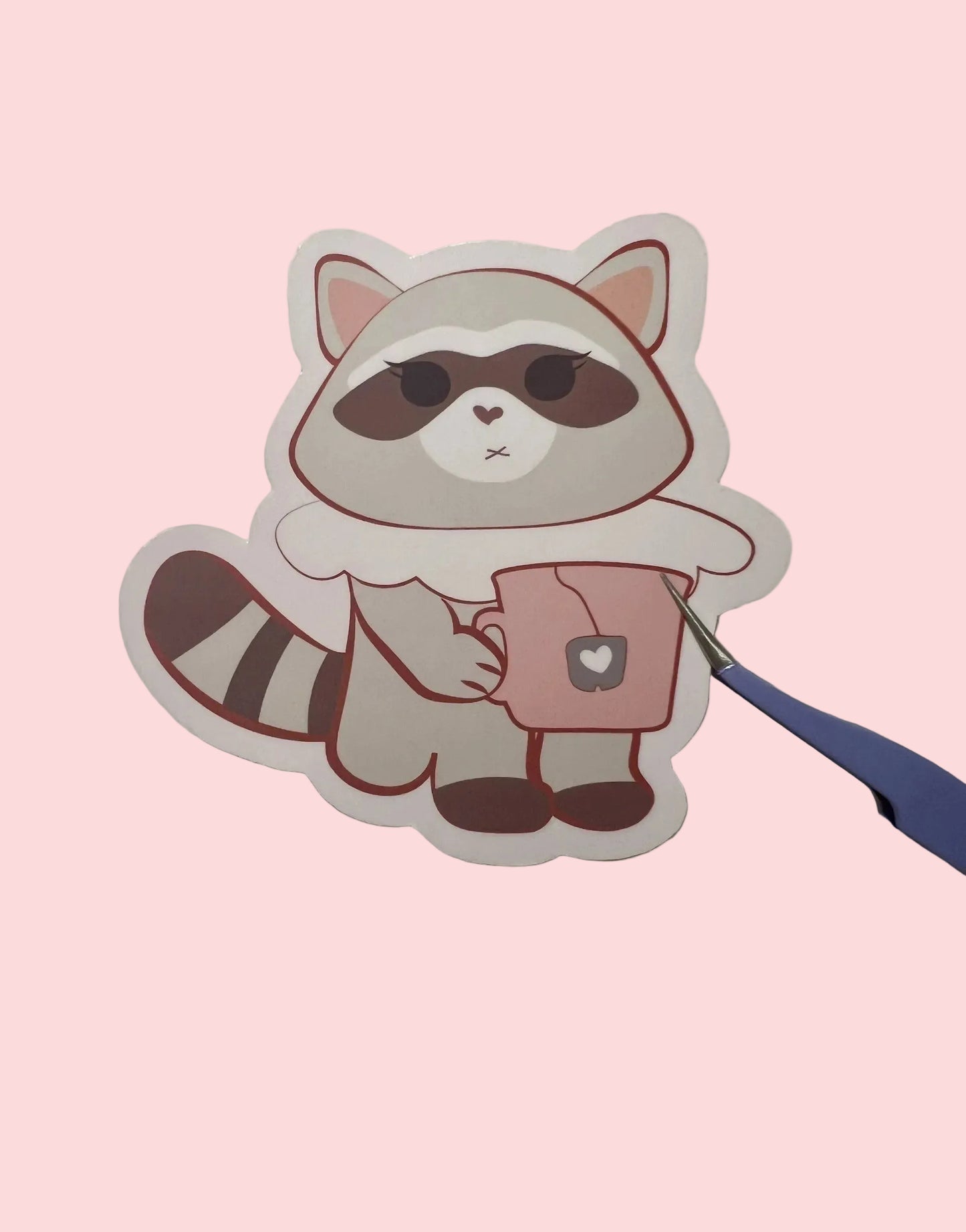 Cartoon raccoon sticker with a cup held by a hand, on a beige background.

