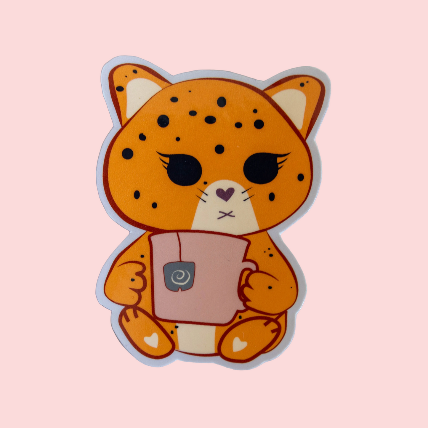 A cute sticker or decal of an orange jaguar cat holding a pink mug, shown on a solid pale pink background.