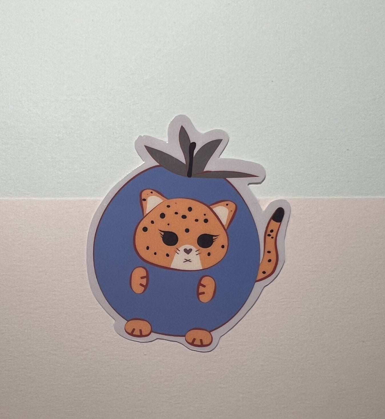 Die-cut Sticker of a kawaii orange jaguar in a blueberry outfit on a light gray background 